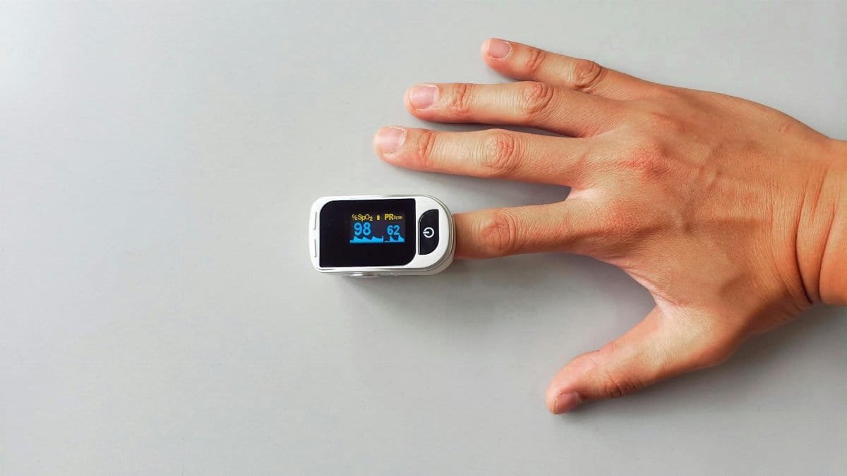 A close-up image of a hand wearing a pulse oximeter, showing health metrics.