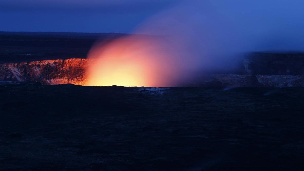 A stunning nighttime view of a volcano eruption, with fiery lava glowing against the dark sky.
