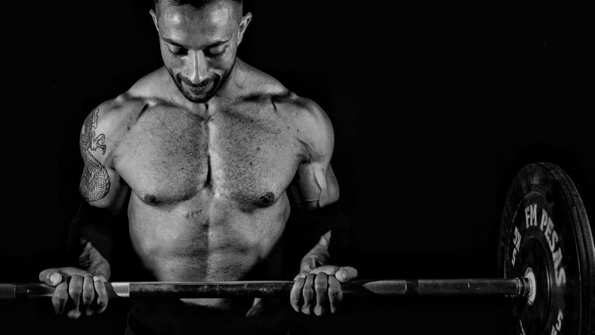 Dramatic black and white photo of a muscular man lifting weights, focusing on strength.