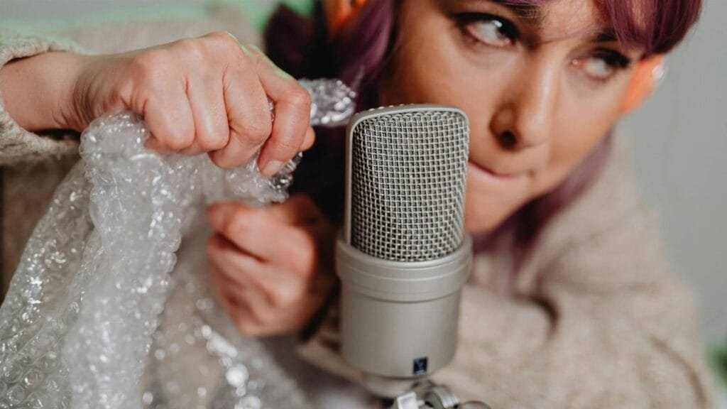 Close-up of a woman creating ASMR sounds with bubble wrap and a microphone.