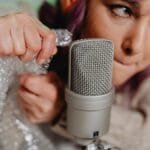 Close-up of a woman creating ASMR sounds with bubble wrap and a microphone.