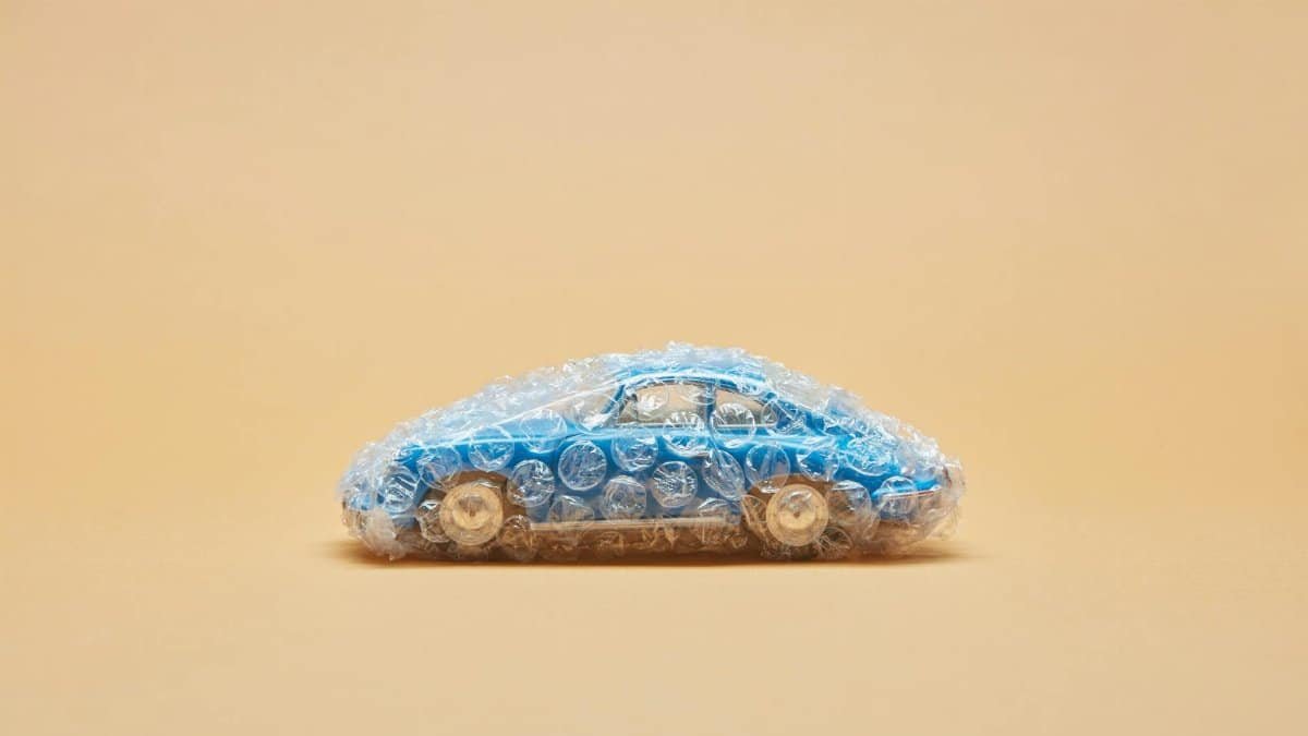 Blue toy car wrapped in bubble wrap against a beige background, minimalist concept.