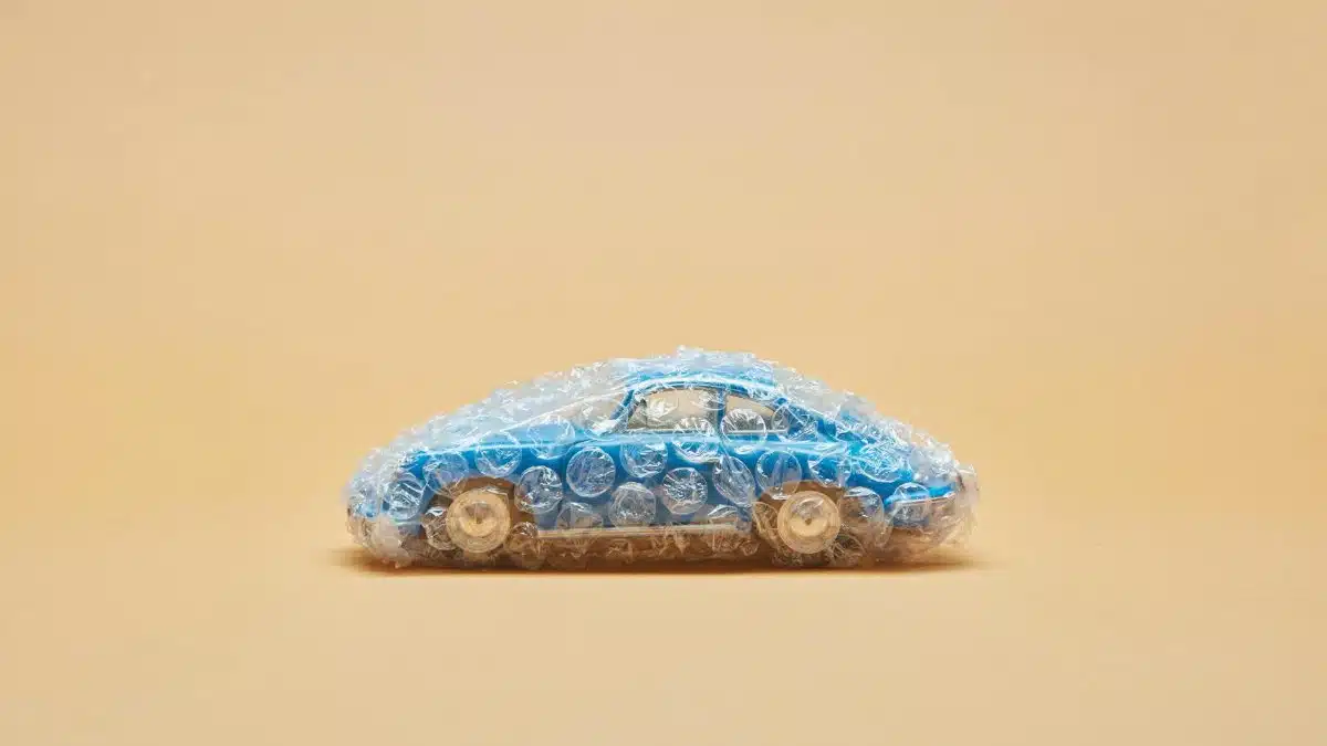 Blue toy car wrapped in bubble wrap against a beige background, minimalist concept.