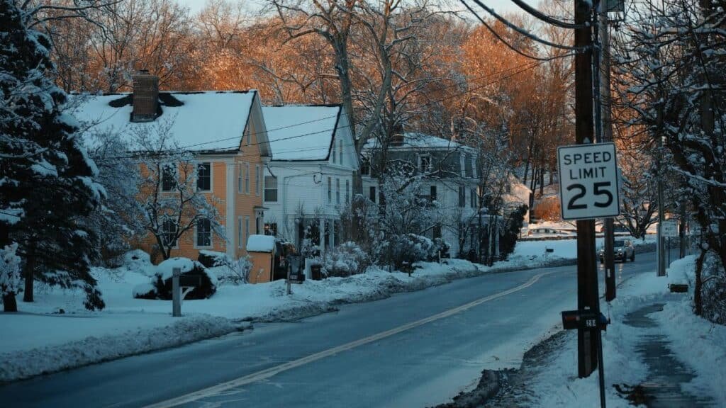 Winter view of a picturesque snowy street with colorful houses and a speed limit sign in a village.