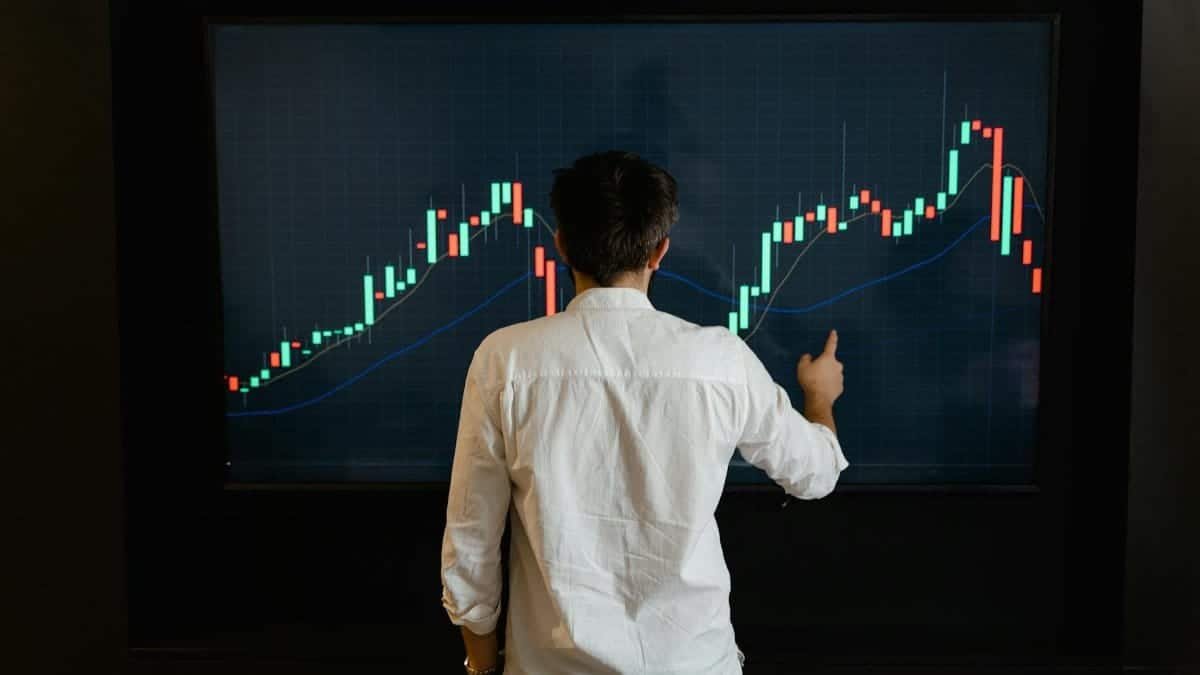 Adult male reviewing stock market data on a large display screen indoors.
