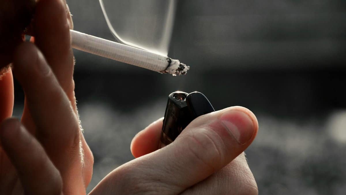 Detailed image of hands holding a cigarette and lighter, emphasizing smoking habit.