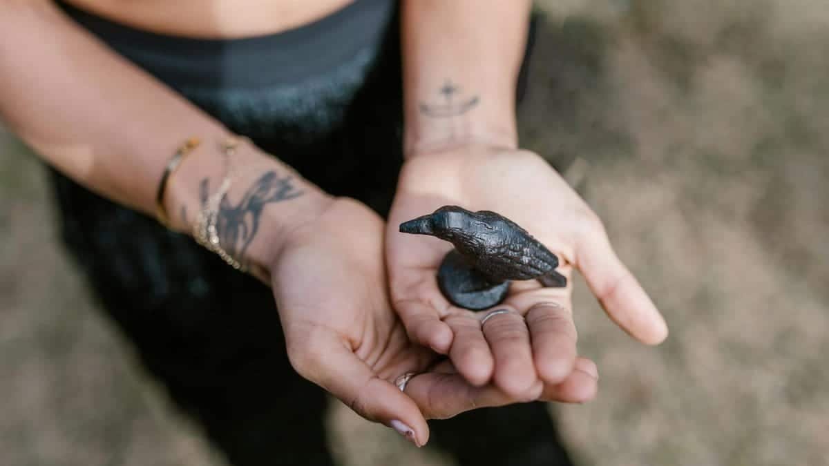 Close-up of hands holding a raven statue, symbolizing magic and spirituality outdoors.