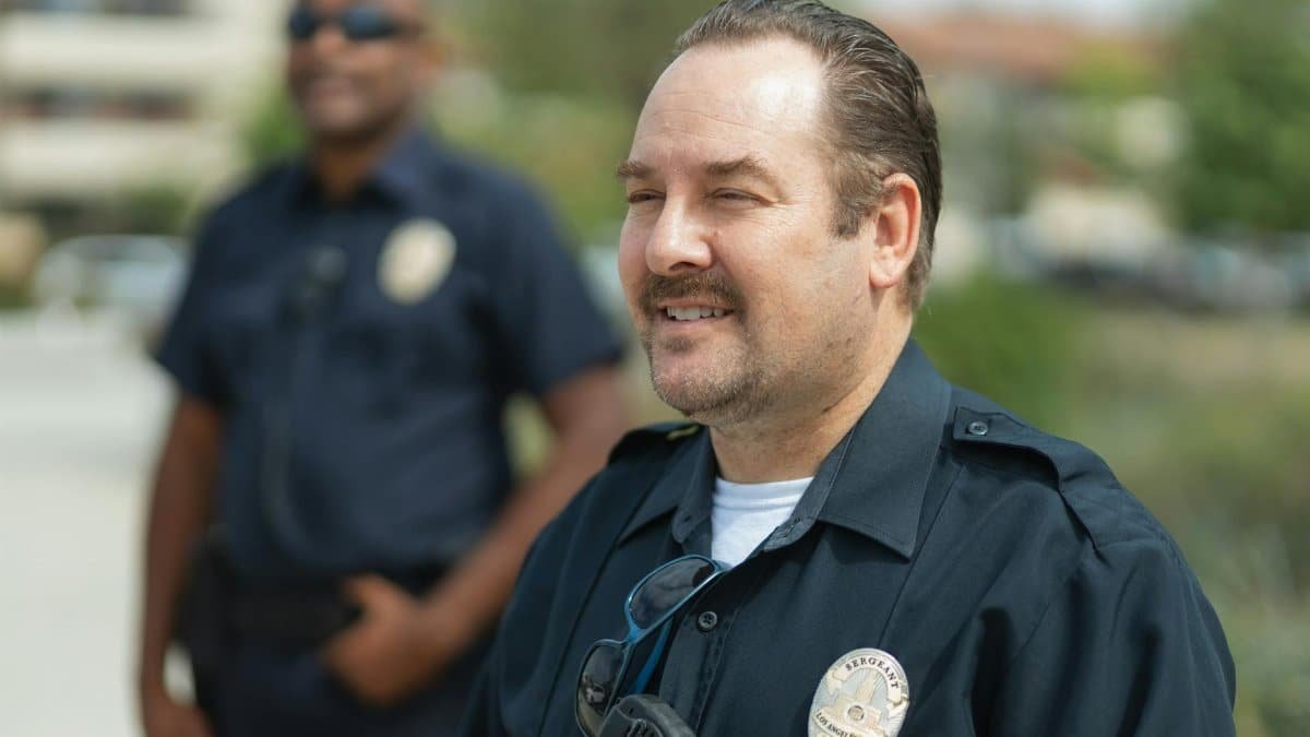 Two police officers smiling outdoors in uniform, representing community service.