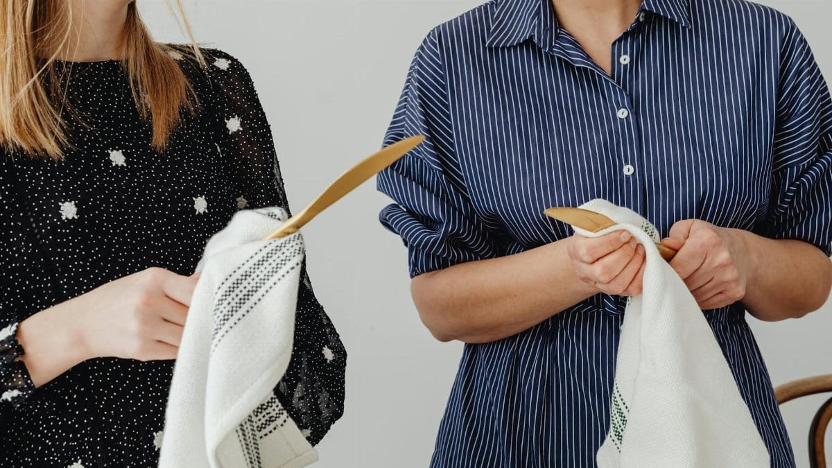 Two women cleaning wooden spoons with towels in a kitchen setting, showcasing domestic life.
