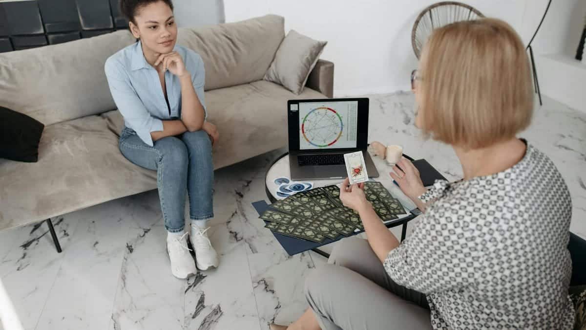 Women discuss astrology with a natal chart and tarot cards on a couch.
