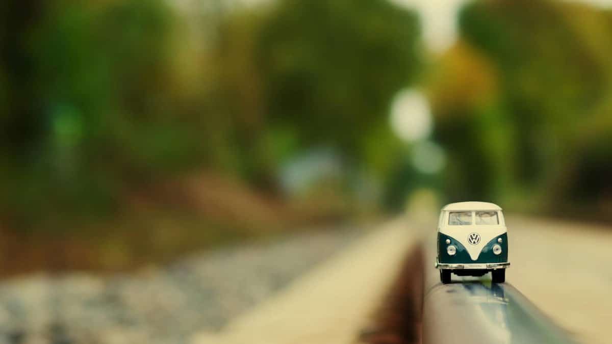 A miniature vintage VW bus toy car sits on a railway track, blurred background.