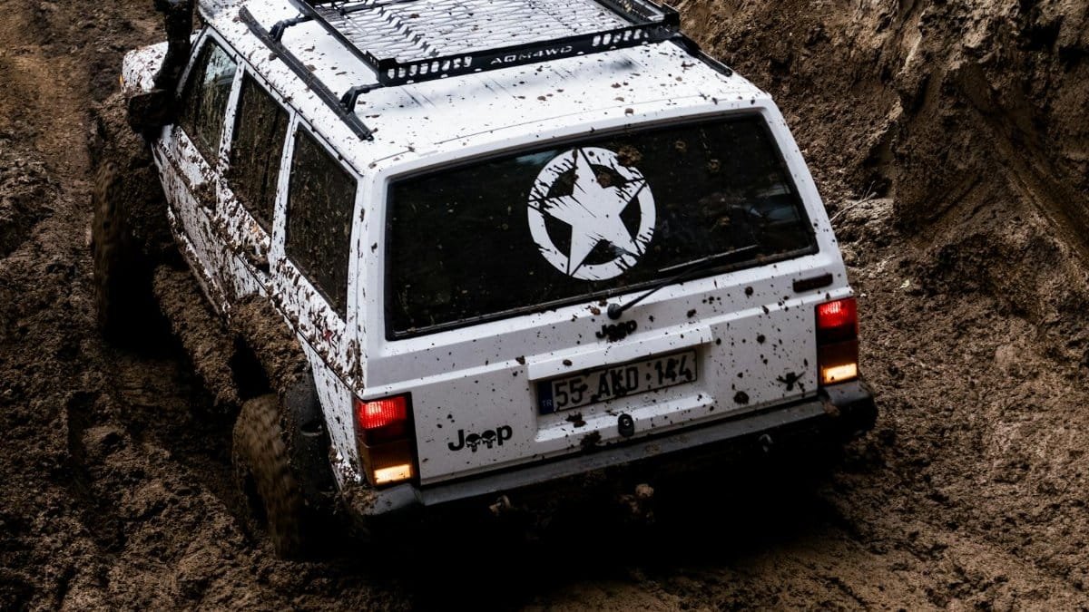 White Jeep Cherokee navigating through muddy terrain, showcasing off-road capability and adventure spirit.