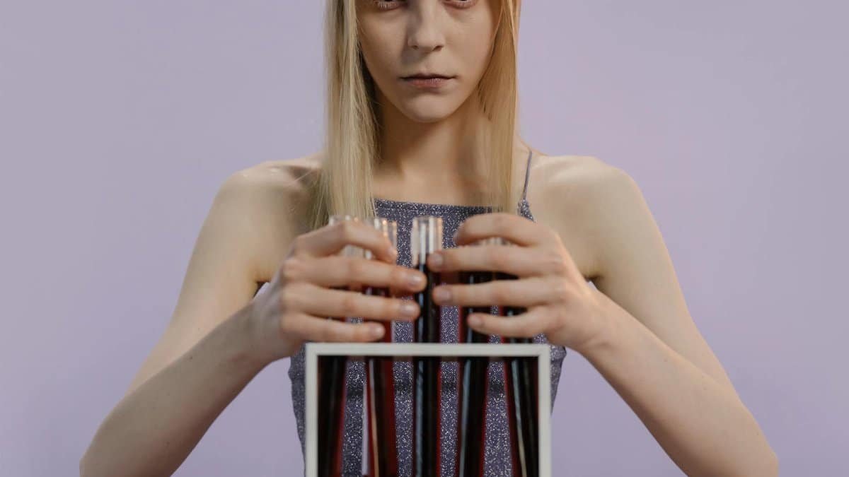 Conceptual portrait of a woman holding test tubes filled with red liquid, exuding a mysterious and eerie vibe.