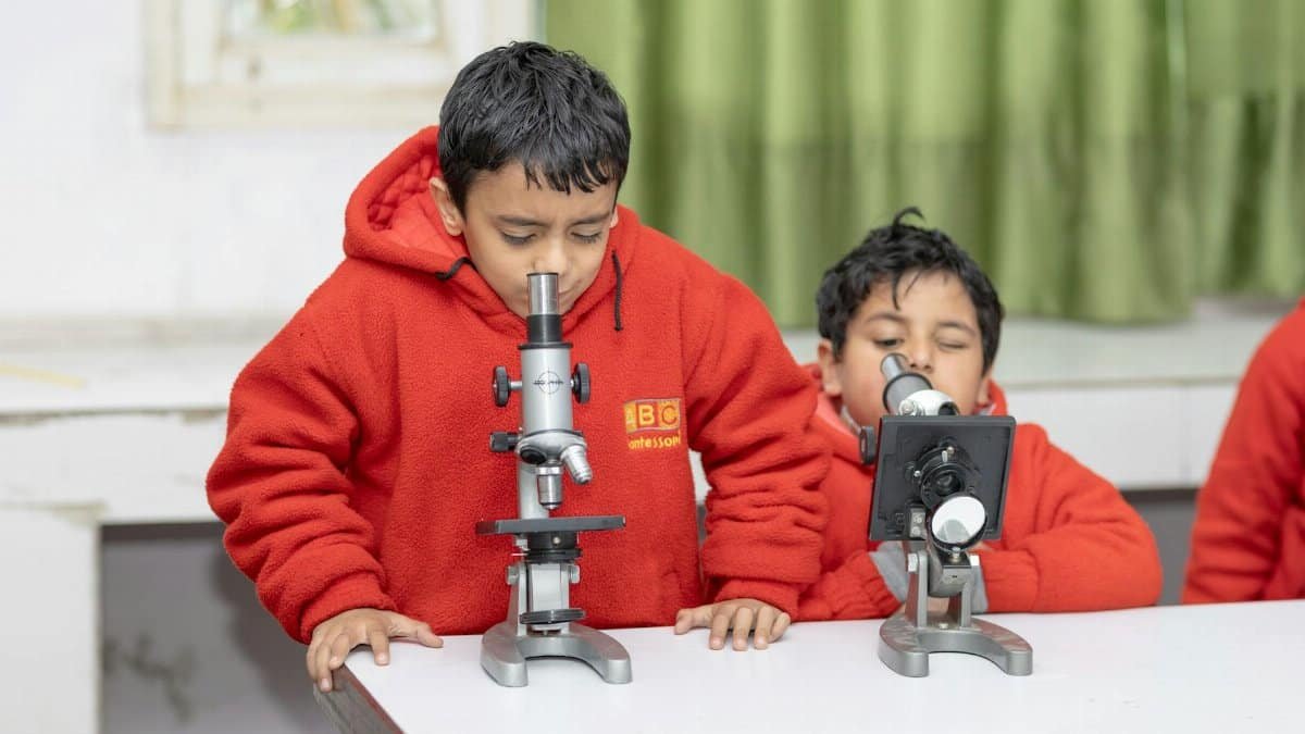 Two children in red hoodies using microscopes in a classroom setting, focusing on scientific exploration.