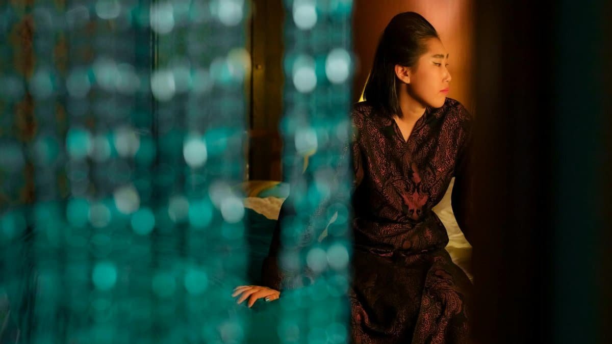 Asian woman sitting thoughtfully behind a beaded curtain, creating a serene indoor ambiance.