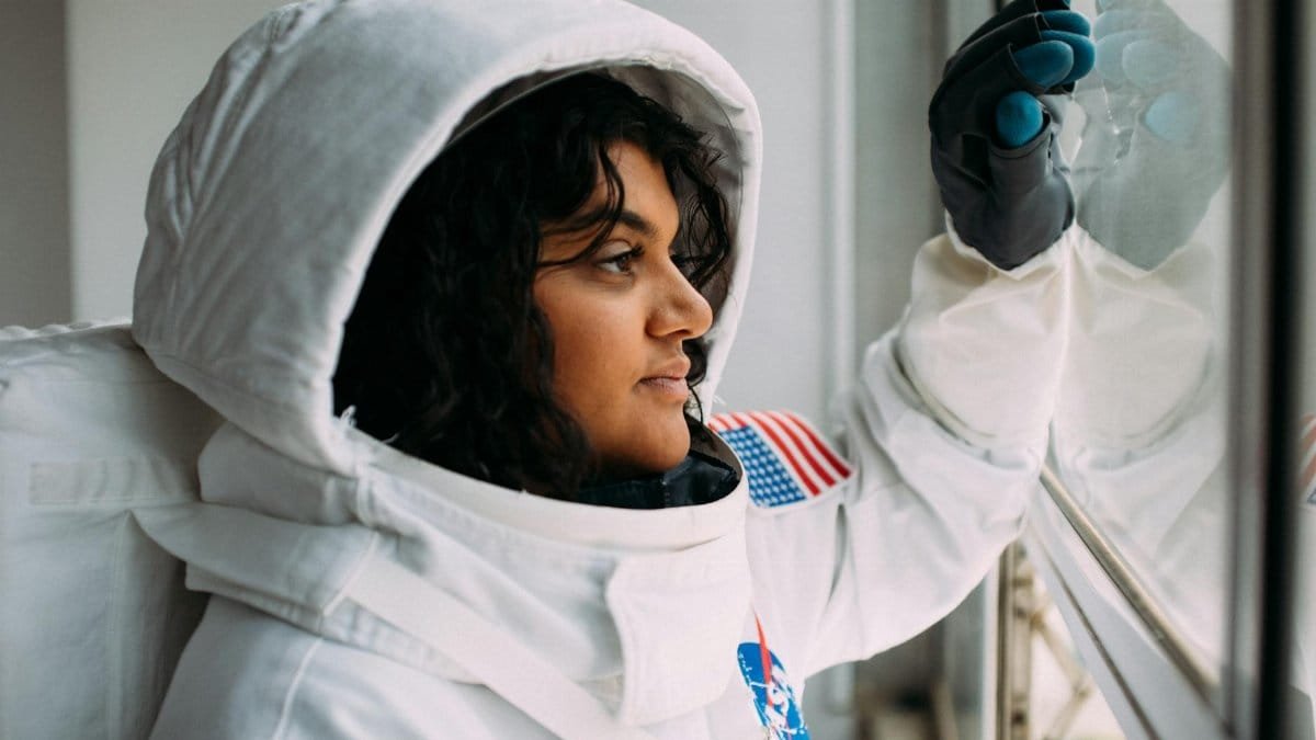 A woman in an astronaut suit looks thoughtfully out of a window, embodying space exploration dreams.