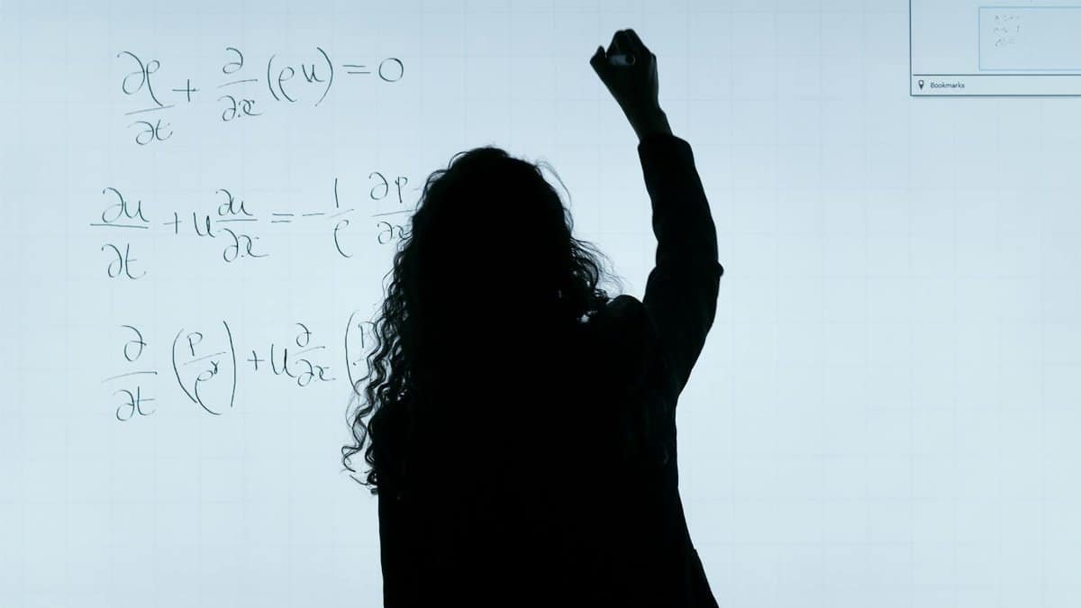 A silhouette of a woman writing mathematical equations on a large whiteboard, representing education and analysis.