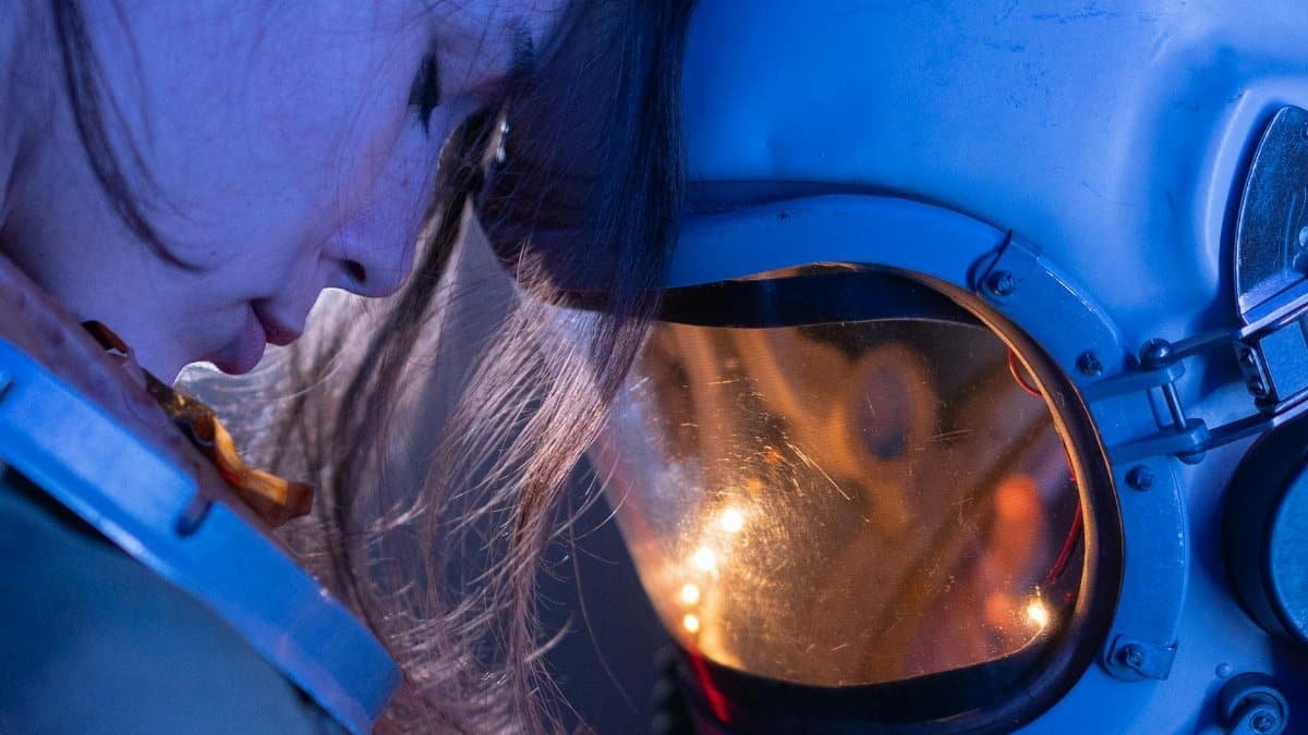 Close-up of a woman in a reflective moment with a space helmet, conveying emotion and futuristic themes.