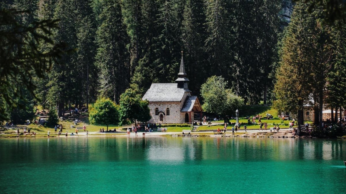 A picturesque church by a serene lake surrounded by lush forest, offering a peaceful countryside view.