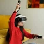 Woman using VR headset and controllers while gaming in a cozy living room setting.