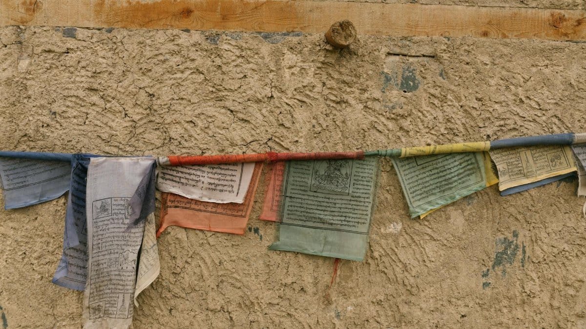 Colorful Tibetan prayer flags with sacred texts on a textured wall, symbolizing peace and spirituality.