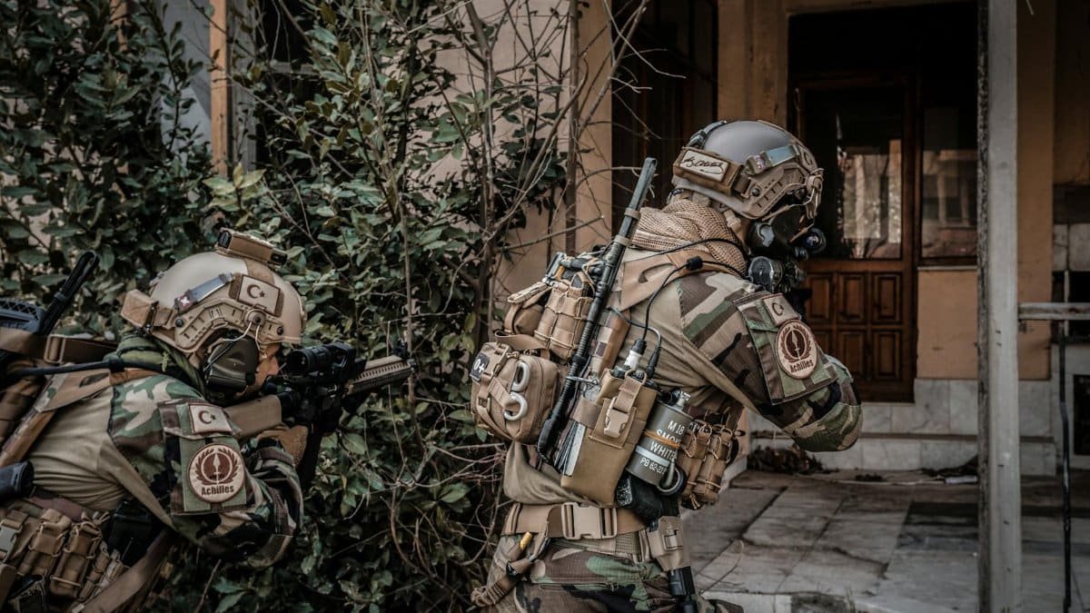 Two soldiers in camouflage advance with rifles during an urban military mission.