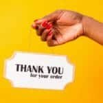 A hand holding a thank you sign on a bright yellow background, expressing gratitude.