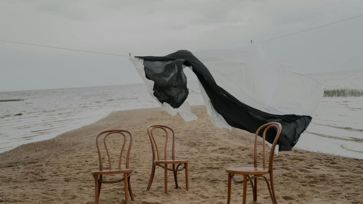 Three chairs on a sandy beach with laundry fluttering in a breezy sky.