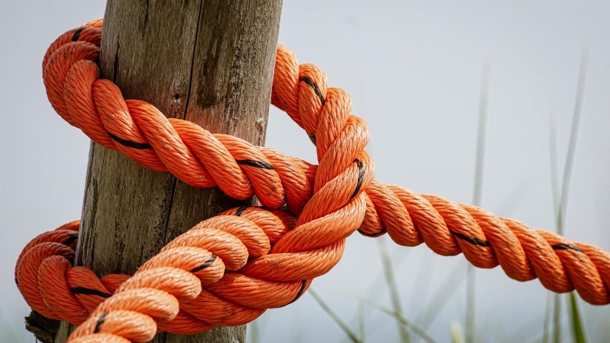 Detailed view of a bright orange rope tied securely around a weathered wooden post in an outdoor setting.