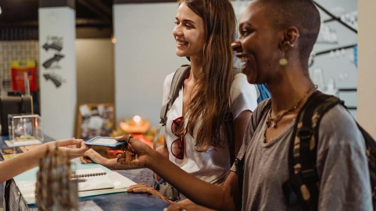Two women enjoying a cheerful check-in at a hostel reception desk.
