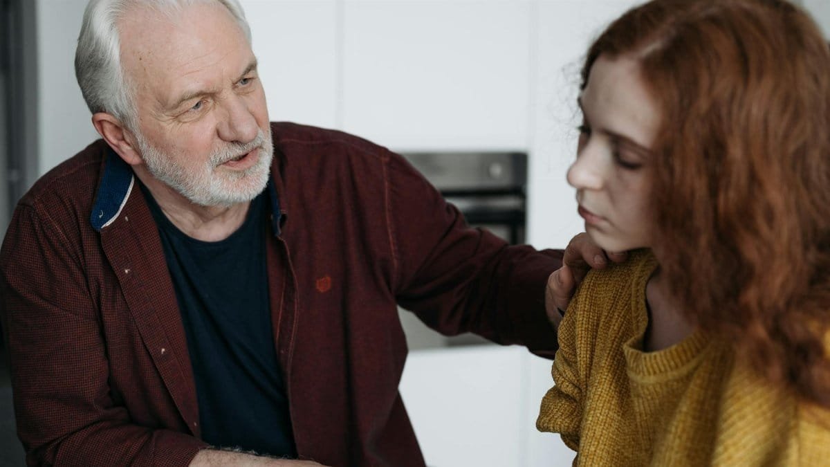 An elderly man consoles a young woman indoors, expressing empathy and understanding.