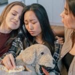 Three women sitting together, sharing popcorn and comfort. Emotional bonds and friendship.