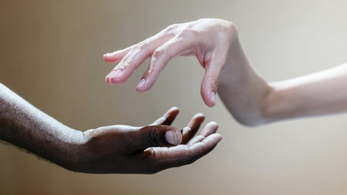 Two people reaching out, symbolizing unity and diversity through the touch of hands.