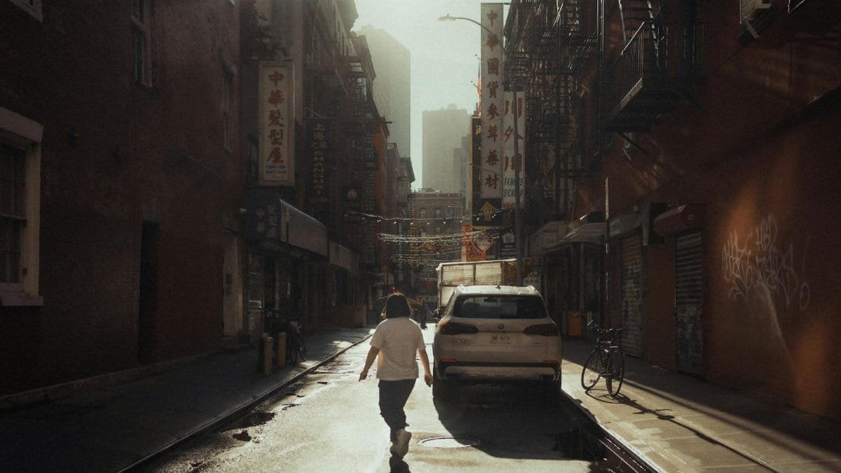 A person walking down a twilight street in Chinatown, New York City, with vibrant signs and urban architecture.