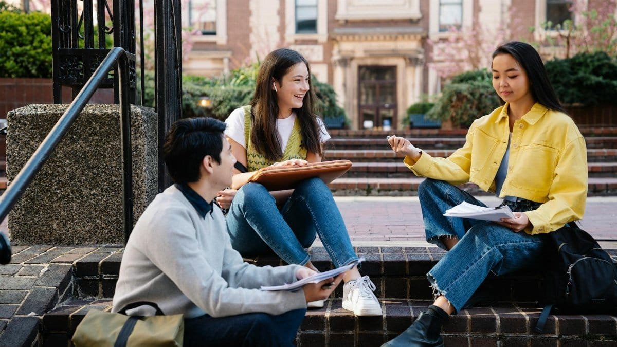 A group of college students sitting and discussing on university steps, engaging in lively conversation.