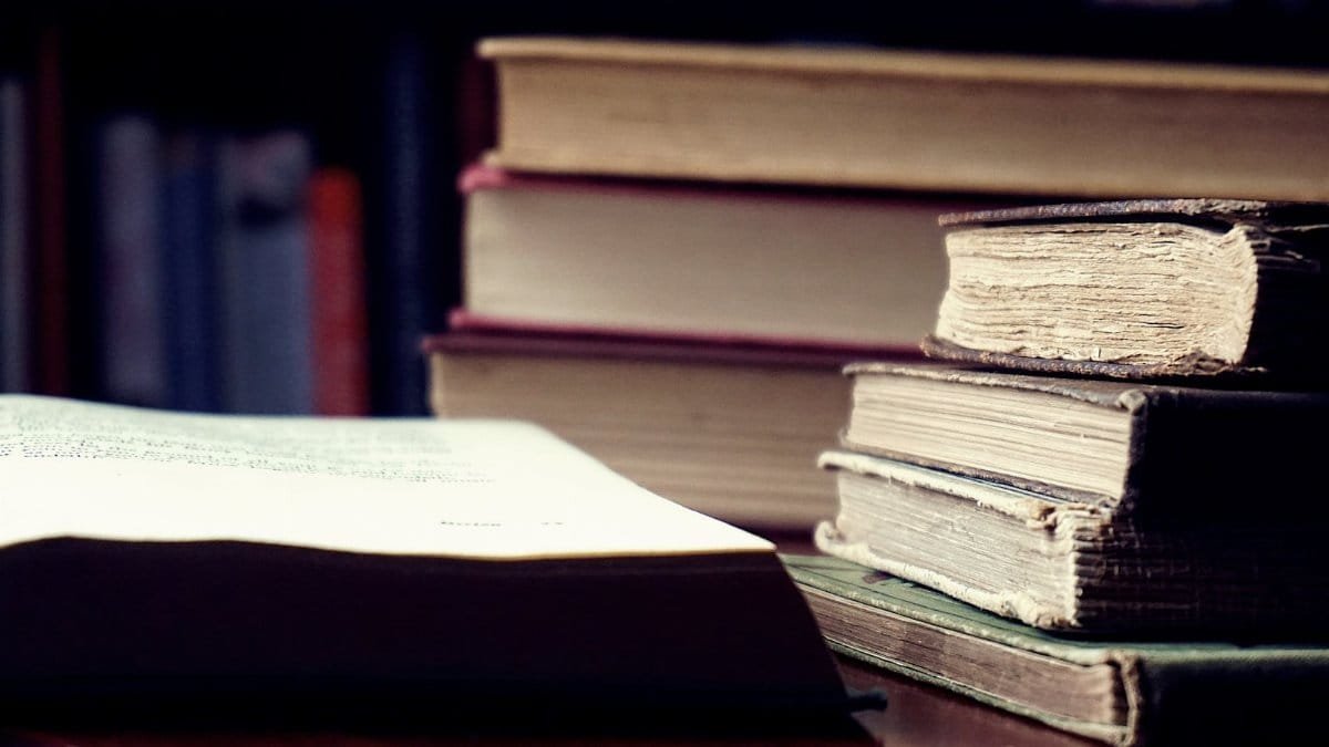 A stack of vintage hardcover books in a dimly lit library setting symbolizes knowledge and wisdom.
