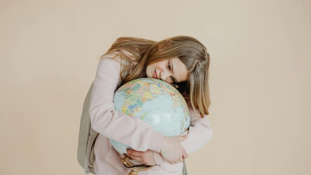 A young girl in a studio holding and hugging a globe, symbolizing global connection and love for Earth.