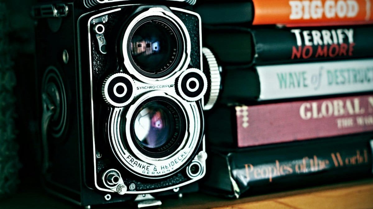 Close-up of a classic Rolleiflex camera beside stacked books, evoking nostalgia and history.