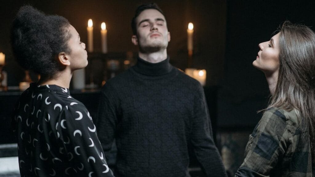 Three individuals engage in a spiritual meditation surrounded by candlelight.