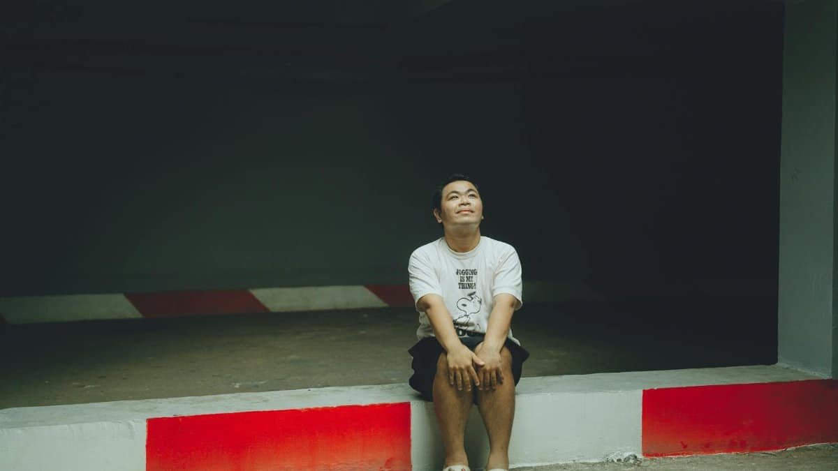 A man sitting thoughtfully in an urban parking area, serene expression.