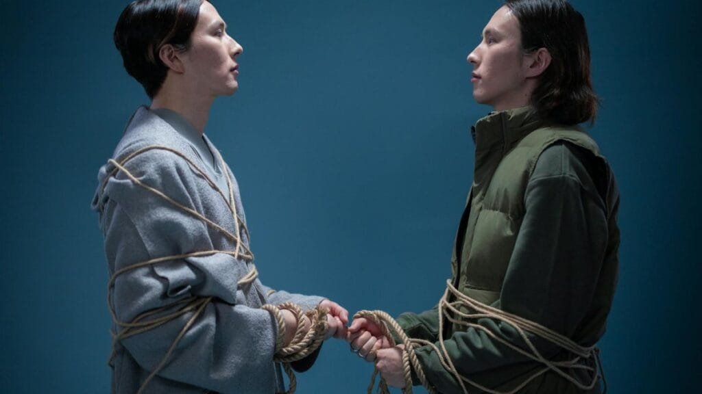 Two individuals tied with rope standing face-to-face on a blue background.