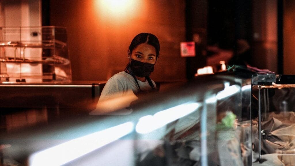 Portrait of a masked employee working behind a glass counter, creating a safe service environment in Richmond, Virginia.