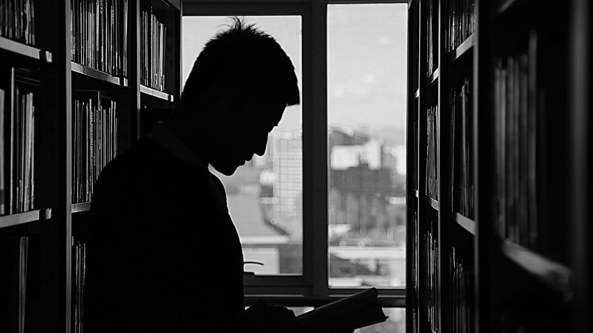A moody silhouette of a man reading in a library, capturing solitude and contemplation.