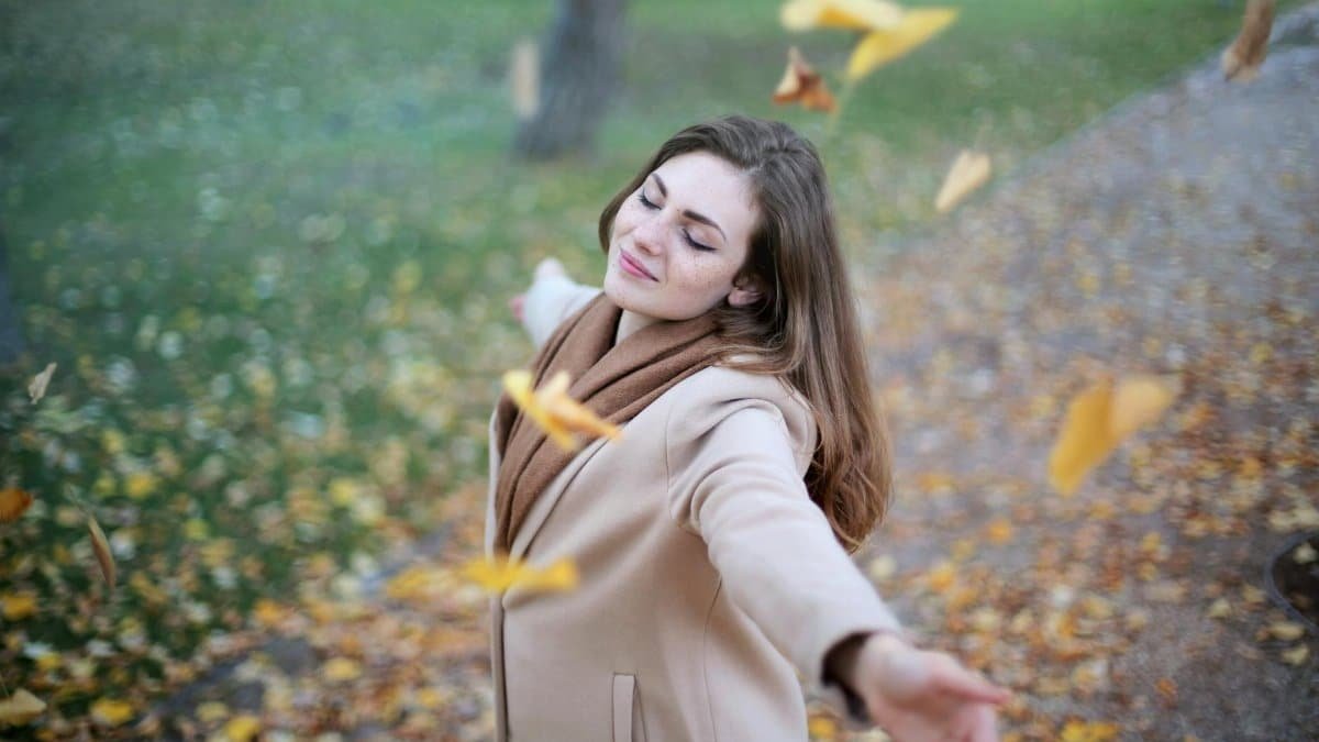 Young woman with arms outstretched, delighting in fallen leaves in a Paris park during autumn daytime.
