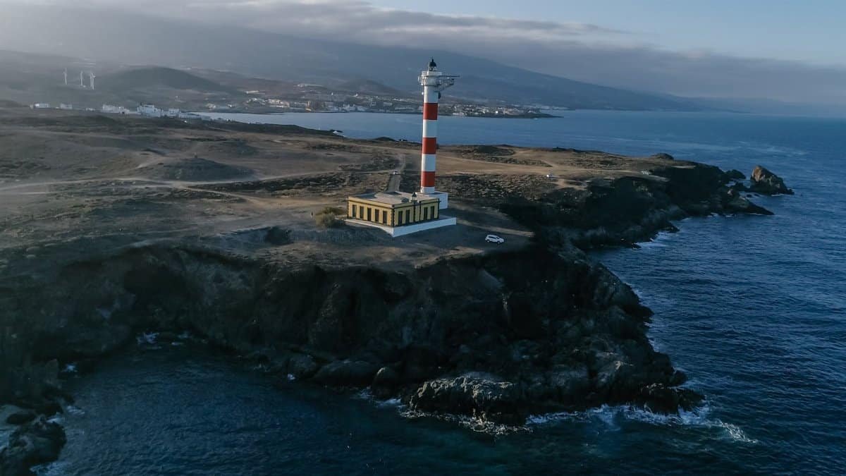 Drone capture of lighthouse perched on a rocky coast against sea and sky.