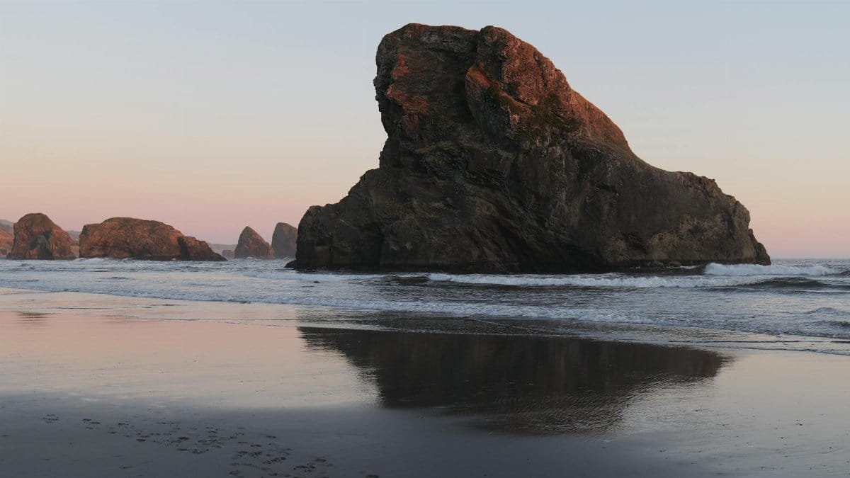 Captivating view of a dramatic rock formation by the sea during sunset, reflecting in the water.