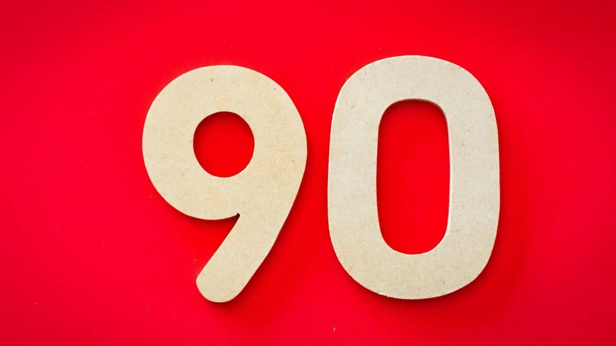 Minimalist depiction of wooden numbers '90' against a vivid red backdrop, capturing simplicity and elegance.