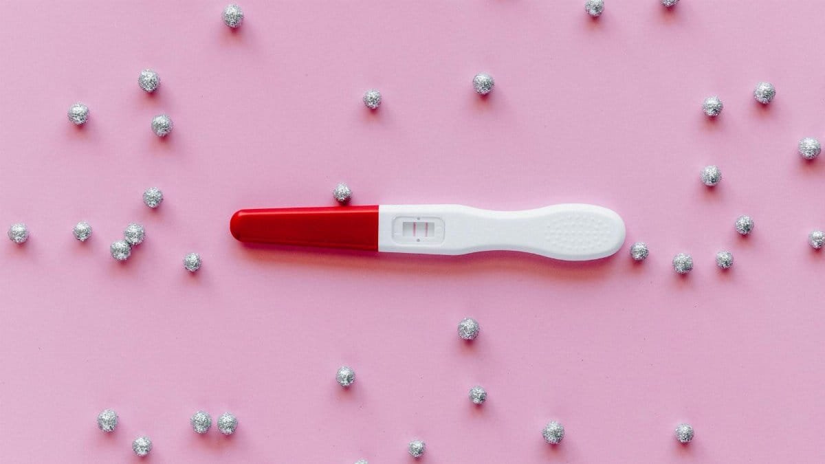 Positive pregnancy test with double lines on a pink background with silver decorations.