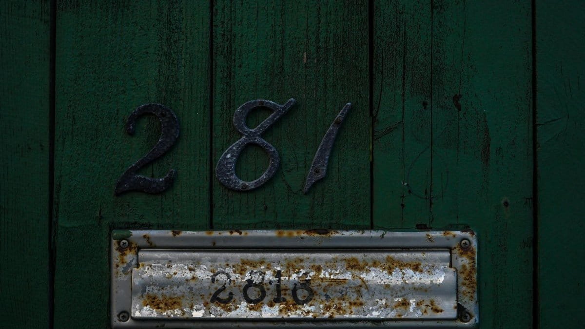Close-up of a green wooden door with rusty mailbox and house number 281.