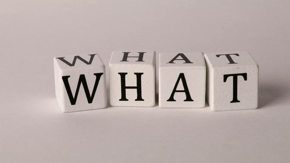 Close-up of wooden blocks with letters spelling 'What' on a white background, emphasizing curiosity and inquiry.